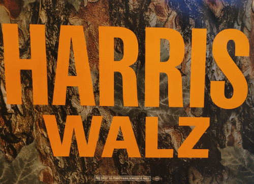 It's got Harris and Walz
printed in pretty bright orange letters, while the background looks like tree bark. So, if you hung the sign on a pine
tree, it would kind of look like the letters were printed on the tree