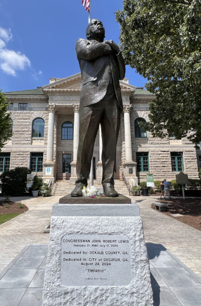 A 12-foot-tall-size statue of John Lewis
clasping his hands over his chest, sitting on a 3-foot inscribed stone pedestal