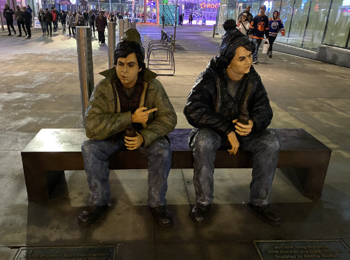 Two bronze-but-painted statues
of the characters sitting on a park bench in an open-air mall