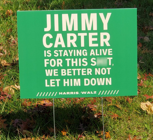 It says 'JIMMY CARTER IS STAYING ALIVE FOR THIS S**T, WE BETTER NOT LET HIM DOWN. HARRIS/WALZ'