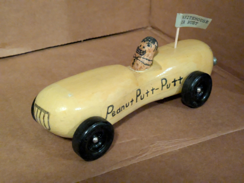 A peanut-shaped car
with a peanut in the driver's seat and a flag that says 'White House or Bust'