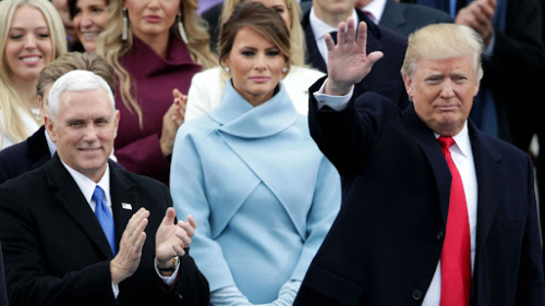 Melania Trump stands behind her husband, frowning